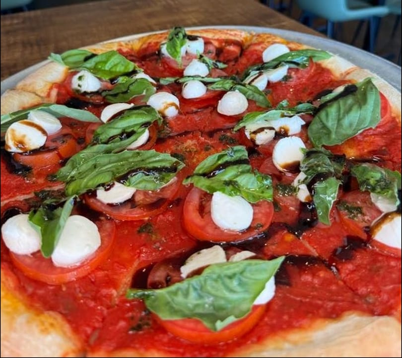 Caprese pizza with fresh tomatoes, mozzarella, basil, and balsamic glaze on a red sauce base.